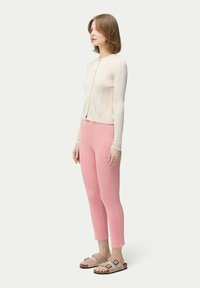 Krämfärgad ribbad cardigan, rosa ribbade byxor och bruna sandaler. Outfiten har en figurnära design och mjuk textur, med strukturerade linjer.