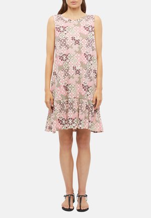 Femme portant une robe sans manches, longueur genou, avec des motifs floraux et géométriques roses et marron, associée à des sandales noires à brides.