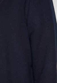 Dunkelblaues Strickpullover-Detailaufnahme, der eine glatte Textur und ein elegantes Design zeigt, mit einer taillierten Silhouette und gleichmäßigem Stich.