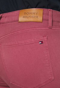 Rosa denimjeans med en läderetikett från Tommy Hilfiger på midjan, med en liten logotag på bakfickan och kontrasterande sömmar.