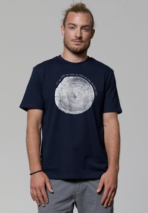 Navyblauwe katoenen t-shirt met een cirkelvormige boomringgrafiek in het wit, met omringende tekst. Korte mouwen, ronde halsontwerp, relaxte pasvorm.