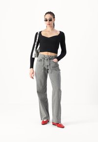 Top corto de manga larga de canalé negro, jeans de pierna ancha grises con cordones y zapatos de punta roja. Accesorios: bolso de mano plateado y gafas de sol.