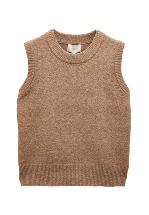 Junge Frau mit glatten braunen Haaren, die ein ärmelloses braunes Stricktop und weiße Hose mit Kordelzug trägt, steht vor einem einfarbigen beigen Hintergrund.