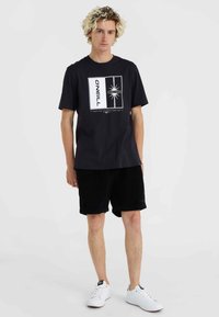Black cotton t-shirt featuring a graphic print with a star motif, paired with black corduroy shorts and white sneakers.