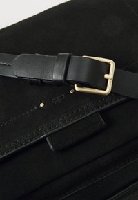 Borsa in suede nera con un manico in pelle nera dotato di fibbia dorata. I dettagli di cucitura e hardware notevoli arricchiscono il design complessivo.