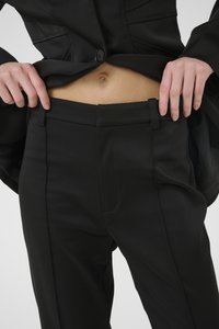 Čierne nohavice na mieru vyrobené z hladkej tkaniny majú plochý pás, bočné vrecká a elegantný dizajn rovného strihu, skombinované s čiernym sákom.