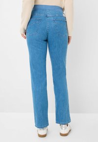 Jean droit bleu clair avec une taille extensible, deux poches arrière et une texture légèrement usée. Porté avec des baskets blanches.