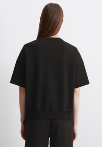 Černá oversized mikina s nízkými rameny, texturovanou tkaninou a žebrovaným lemem. Zadní strana je jednobarevná bez dalších ozdob.