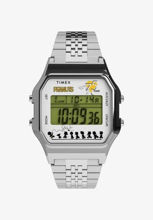 Digitális Timex óra szürke fém szíjjal, téglalap alakú tok, zöld kijelző, "Peanuts" logó, és karakter sziluettek az alján.