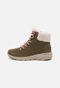 Botte d'hiver en suede vert olive avec des lacets roses, un col en fausse fourrure blanche et une semelle beige mouchetée, conçue pour les conditions froides en extérieur.