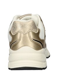 Sneaker met een witte mesh bovenkant, gouden accenten op de hiel en de kraag, een gestructureerde gouden achterkant en een dikke witte zool met zwarte loopvlakken.