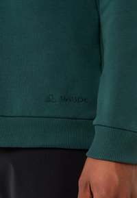 Grüne Sweatshirtjacke mit gerippten Bündchen und Saum, aus weichem Material gefertigt. VAUDE-Logo auf der unteren Vorderseite bestickt.