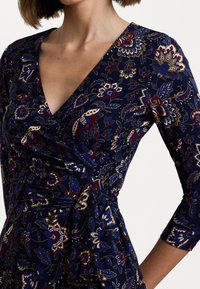 Abito avvolgente blu navy con un motivo floreale caratterizzato da accenti rossi, blu e crema. Design a scollo a V e maniche a tre quarti, legato in vita.