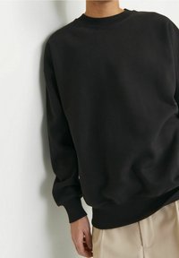 Černá mikina s kulatým výstřihem, dlouhými rukávy a žebrovanými manžetami. Vyrobena z měkké tkaniny, má volný střih a minimalistický design.