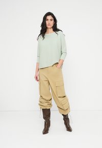 Φωτεινό πράσινο ριμπ τοπ με άνετη εφαρμογή, συνδυασμένο με χακί cargo παντελόνι με τσέπες και καφέ μπότες μέχρι το γόνατο.