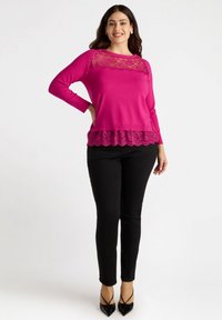 Top fucsia con maniche lunghe, dettagli in pizzo sul collo e bordo in pizzo all'orlo, abbinato a pantaloni neri aderenti e tacchi a punta neri.