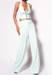 Mátově zelený halter top s hlubokým výstřihem do V a s pěti knoflíky, doplněný širokými kalhotami ze stejného materiálu, které mají hladkou texturu.
