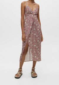 Maxikleid in staubigem Rosé mit floralem Muster, verstellbaren Spaghetti-Trägern, verdrehtem Vorderteil und einem hohen Schlitz bis zum Oberschenkel. Sandalen runden das Outfit ab.