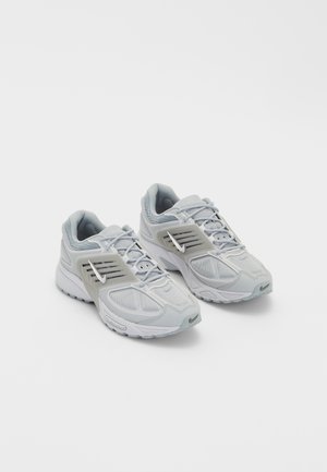 Paire de baskets de sport gris clair avec tiges en mesh, semelles blanches et couvre-lacets latéraux arborant un logo Swoosh blanc.