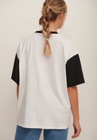 Bawełniana koszulka z luźnym krojem, biała z czarnymi krótkimi rękawami. Tył jest gładki o gładkiej fakturze.