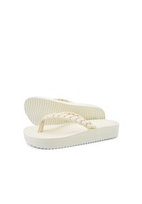 Beige Flip-Flops mit geflochtenem Riemen, einer dicken strukturierten Sohle mit wellenförmigem Muster und einem leicht erhöhten Absatz für zusätzlichen Halt.