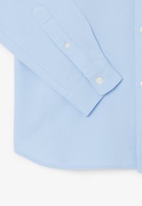 Camicia azzurro chiaro a maniche lunghe, strutturata, con colletto a punta, chiusura con bottoni e polsini regolabili con bottoni bianchi.