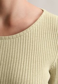 Haut en tricot côtelé jaune clair avec un col large et un tissu texturé. Le motif se compose de côtes verticales, améliorant la flexibilité et l'ajustement.