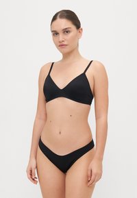 Črn bikini komplet s trikotno zgornjo majico s tankimi nastavljivimi naramnicami in nizkimi ujemajočimi se hlačkami. Gladka tekstura, minimalistična zasnova.