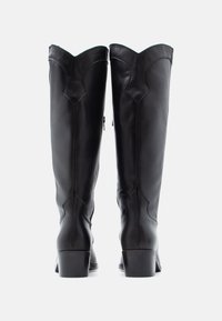 Čierne kožené čižmy po kolená s vrchným okrajom so zvlneným vzorom, vybavené bočnými zipsami a pevnými blokovými podpätkami. Hladká štruktúra s viditeľným prešívaním.