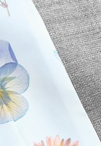 Ziedu auduma fragments ar gaiši zilu fonu, kurā redzami maigi pasteļtoņu ziedi, blakus teksturētai pelēkai vielai.