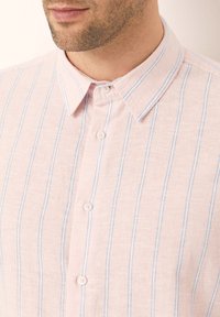 Camisa de botones de color rosa claro con rayas verticales azules, que presenta un cuello clásico y una textura suave. Adecuada para uso casual.