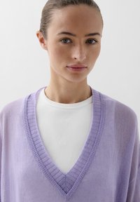 Lila, lichtgewicht trui met een V-hals en ribgebreide randen, over een witte ribgebreide top. Soepele textuur, casual pasvorm en subtiele details.
