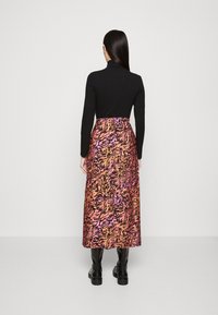 Un col roulé noir associé à une jupe maxi colorée arborant un motif animalier vibrant en orange, rose et noir, ainsi qu'à des bottes noirs arrivant au genou.