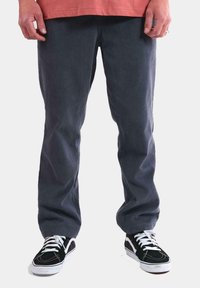 Pantalones de pana grises con una textura acanalada, combinados con zapatillas negras que tienen cordones y detalles en blanco. El dobladillo es recto y sin adornos.