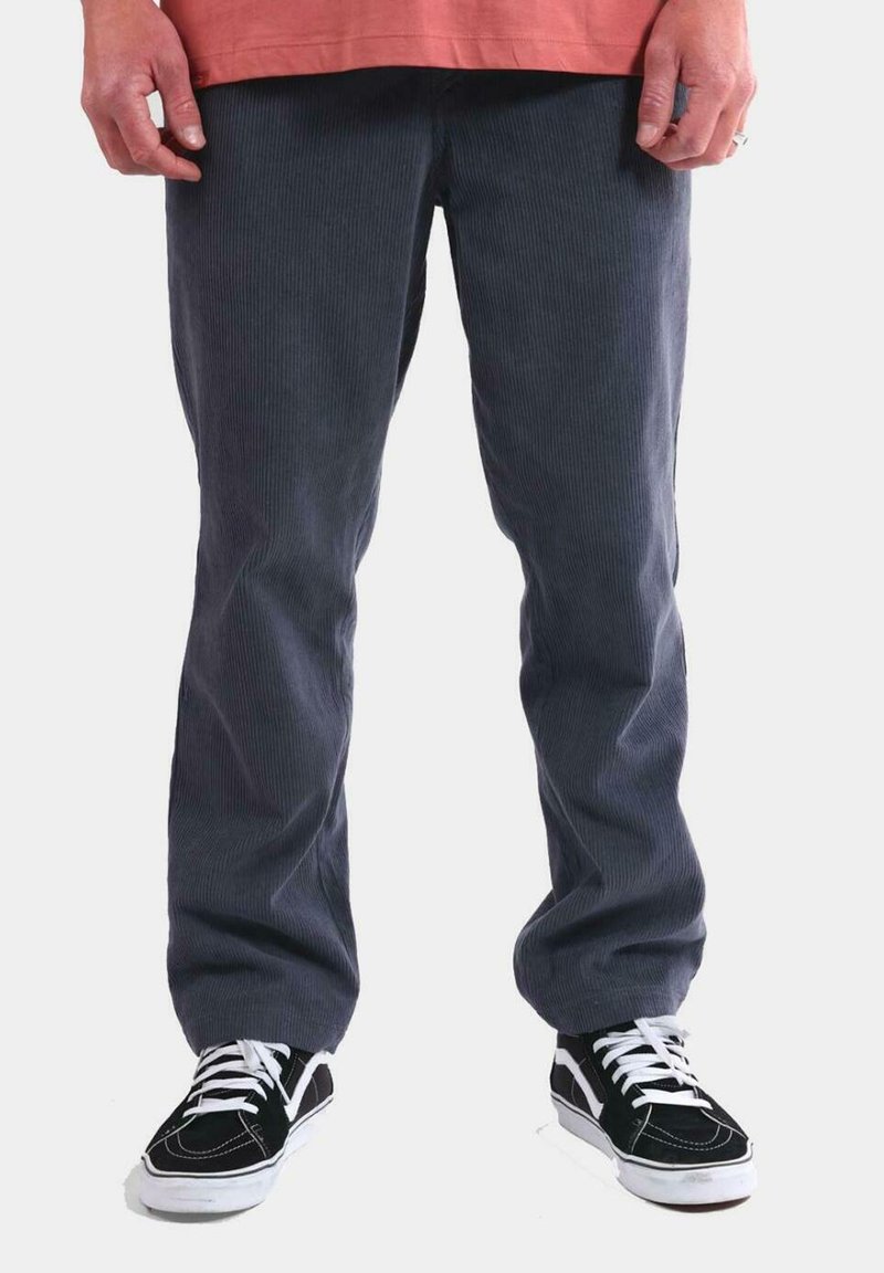 Pantalones de pana grises con una textura acanalada, combinados con zapatillas negras que tienen cordones y detalles en blanco. El dobladillo es recto y sin adornos.