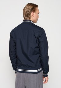 Chaqueta bomber de marina con cuello y puños acanalados de rayas blancas, cintura elástica y tejido suave; presenta un diseño minimalista.