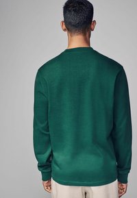 Grünes Langarmhemd aus Strickmaterial, mit Rundhalsausschnitt und lockerer Passform, mit gerippten Bündchen und Saum.