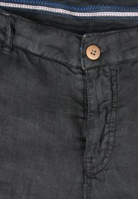 Schwarze Leinenhosen mit einem frontalen Knopfverschluss und einem subtil strukturierten Stoff. Der Innenbund hat bunte gestreifte Akzente.