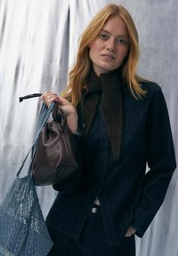 Dunkelblaues Jeanshemd mit Knöpfen, kombiniert mit einer braunen Ledertasche mit Kordelzug und einem hellblauen Netztasche. Mit einem braunen Schal.