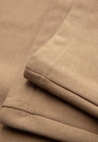 Primo piano di tessuto beige con cuciture fini visibili e bordi piegati, che mostrano la trama e i dettagli della cucitura.