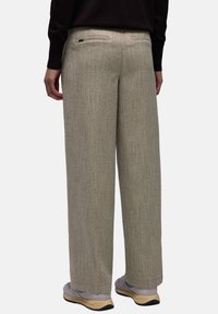 Weite Hose aus einem strukturierten, hellgrauen Stoff. Verfügt über Gesäßtaschen und einen glatten Bund. Kombiniert mit hellen Schuhen.