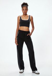 Zwarte cropped sporttop met witte rand, gecombineerd met losse zwarte broek met zijstrepen en een trekkoord in de taille. Witte sneakers.