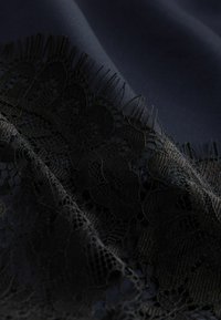 Černý krajkový lem na tmavém látkovém pozadí, zdobený složitými květinovými vzory a jemnou, hladkou texturou.