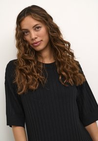 Maglione a coste nero con maniche corte, caratterizzato da un collo dritto e una vestibilità comoda. La texture morbida e una leggera lucentezza sono evidenti.