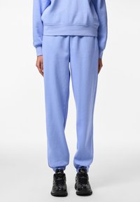 Ljusblå mjukisbyxor i mjukt material med elastisk midja och muddar, kombinerade med svarta träningsskor.