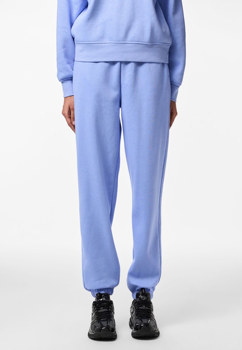 Ljusblå mjukisbyxor i mjukt material med elastisk midja och muddar, kombinerade med svarta träningsskor.