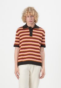 Polo skjorte med flerfarget zigzag-mønster i oransje, hvitt og brunt. Korte ermer og en svart krage med tre knapper.