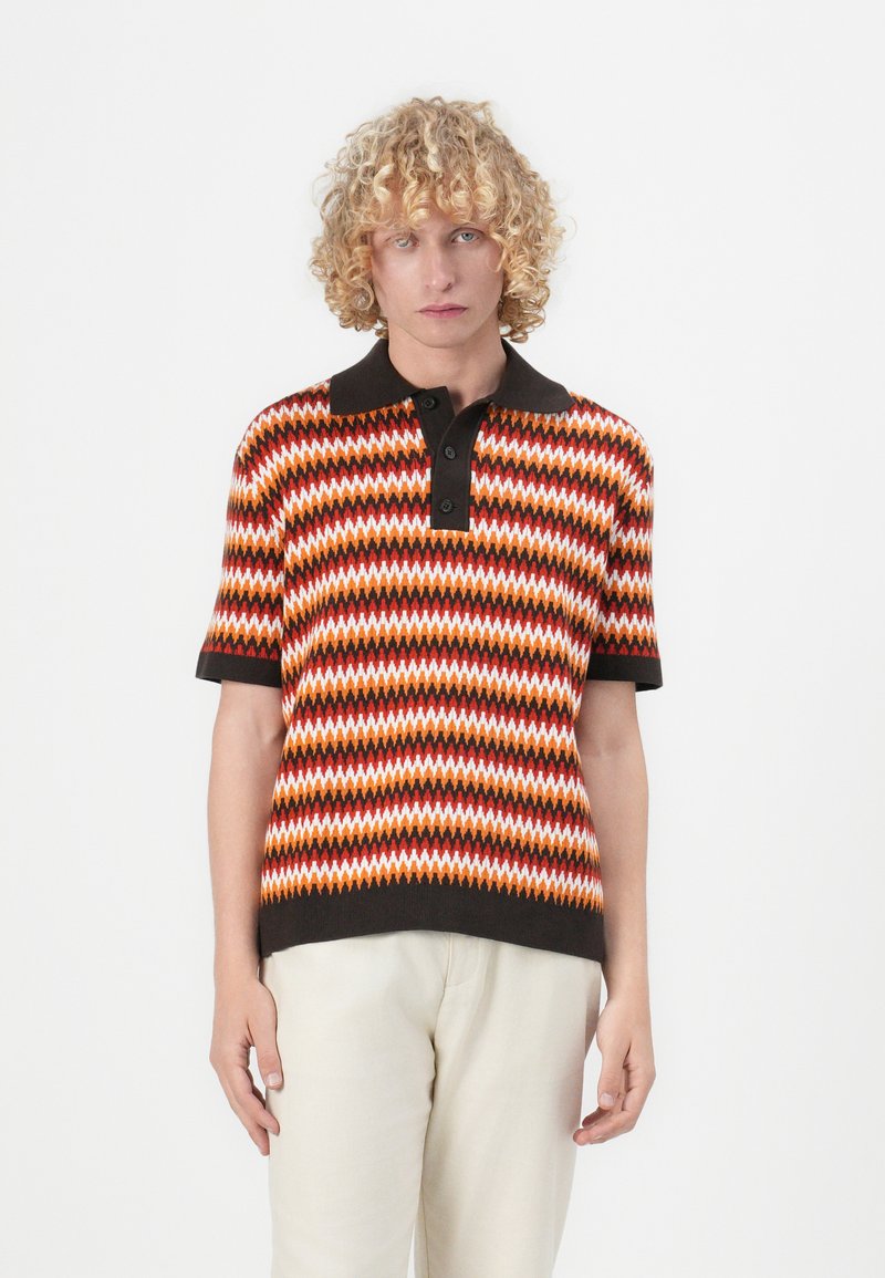 Polo skjorte med flerfarget zigzag-mønster i oransje, hvitt og brunt. Korte ermer og en svart krage med tre knapper.