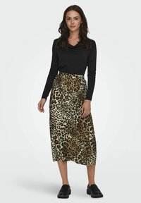 Črn zgornji del s dolgimi rokavi in0 globokim izrezom, združen z midi krilom z leopardjim vzorcem v bež in rjavih odtenkih. Model nosi črne loafers.