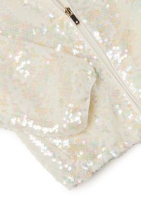 Tessuto di paillettes iridescenti con una base beige chiaro, dotato di chiusura con zip. La texture è liscia e lucida, riflettendo la luce in molteplici colori.
